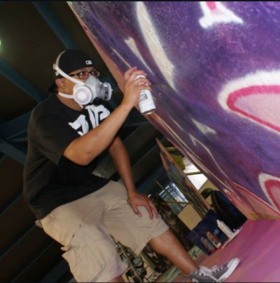 Jay Loo wearing a white protective mask while spray painting a commissioned mural.